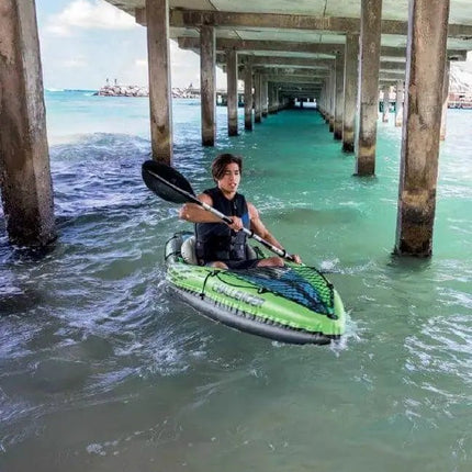Een persoon kajakt onder een betonnen pier in de Intex Challenger K1 Opblaasbare kayak